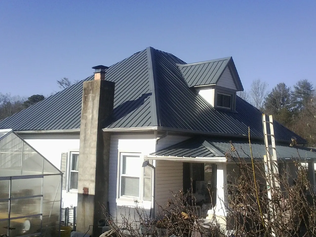 Dark blue standing seam metal roof on a white farmhouse with dormer — Slate & Tile Roof Repair by Roofing Brothers in Tyler