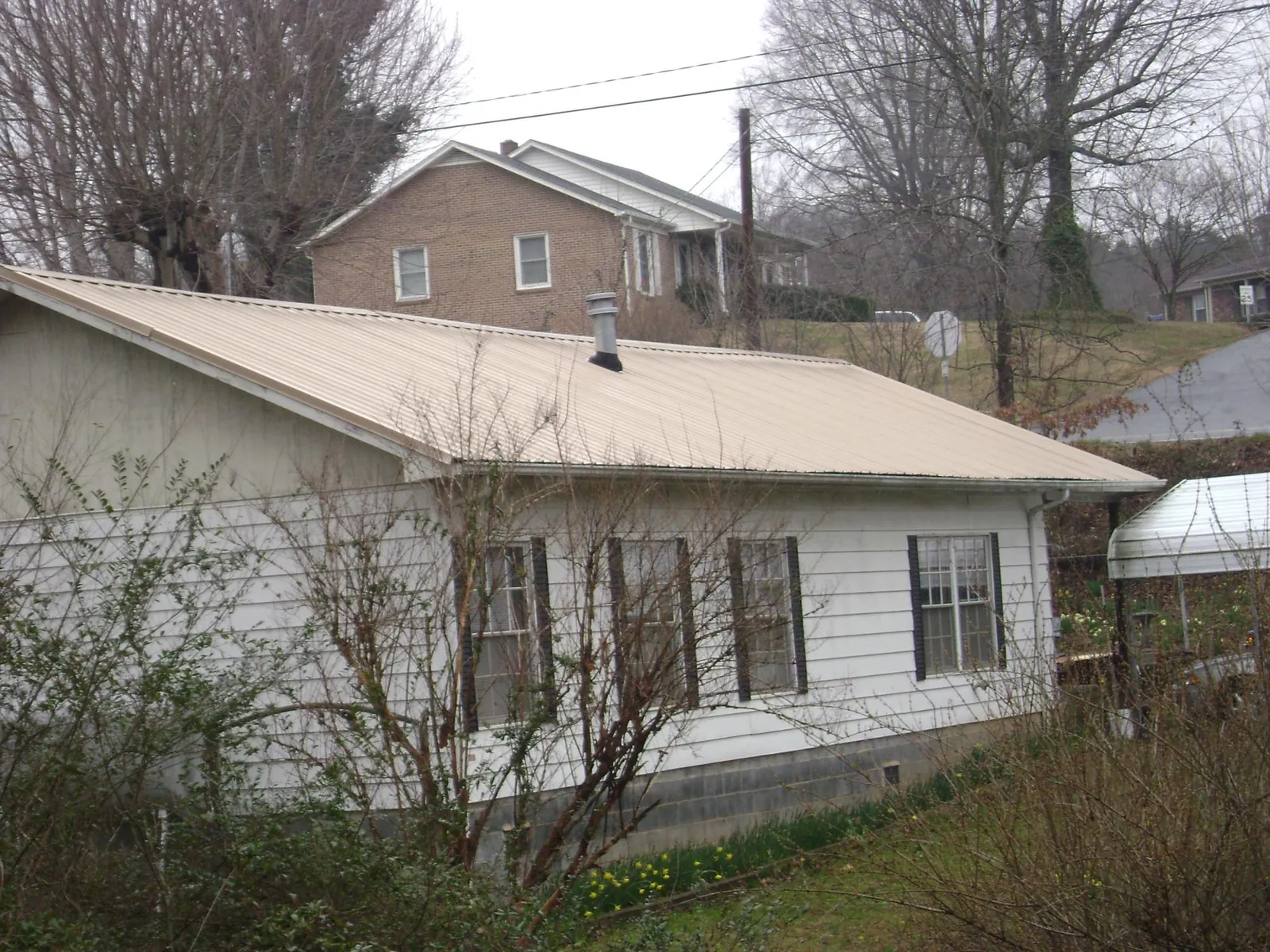 Tan metal roof on a white sided house set into a hillside — Commercial Roofing by Roofing Brothers in Tyler
